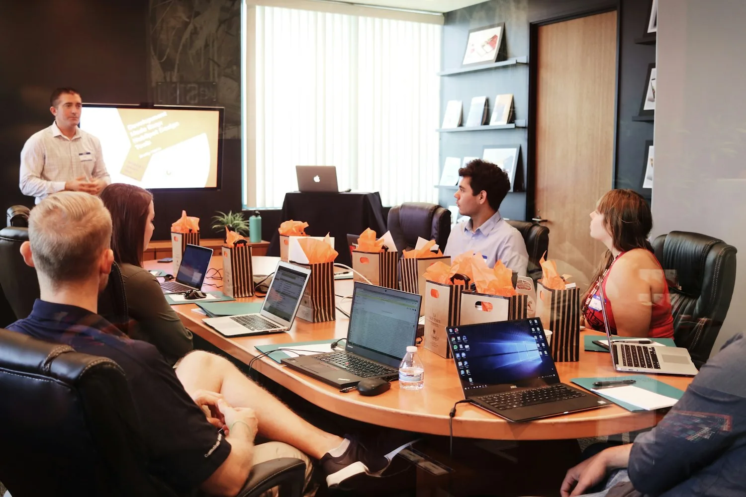 A presenter leads a workshop for colleagues seated around a conference table.